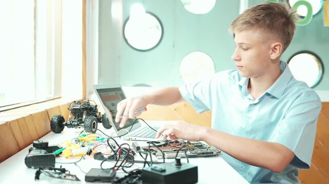 Side view of student looking at laptop screen and fixing electronic board while coding program or programming robot system at STEM class. Caucasian teenager repairing robotic car model. Edification