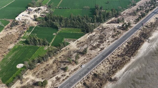 aerial drone footage of a Road stretching through farmland with sparse trees alongside a mudflat area in a rural landscape on a sunny day High quality drone 4k footage