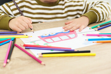 Little boy drawing van with pencil at wooden table, closeup