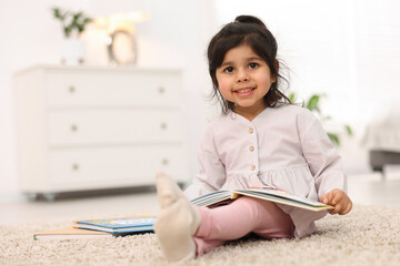 Fototapeta premium Cute little girl reading book on floor at home. Space for text