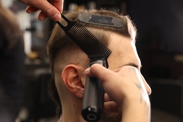 Obraz premium Stylist cutting man's hair with clipper in barbershop, closeup
