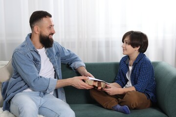 Cute boy greeting his father with gift and holiday card at home