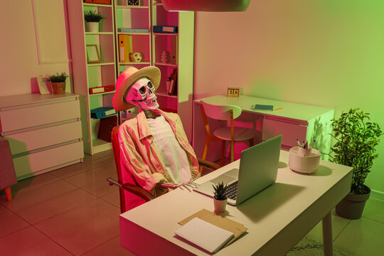 Human skeleton model with summer hat and clothes at desk in dark office