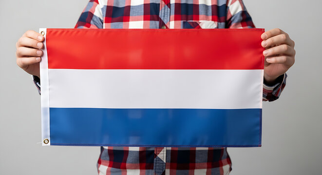 ​A man wearing a checkered shirt holds the Dutch national flag with its red white and blue horizontal stripes.