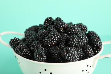 Colander with sweet ripe blackberries on turquoise background, closeup © Pixel-Shot