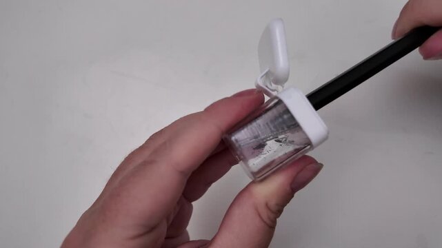 Close-up of a woman's hands sharpening a pencil with a sharpener above a table