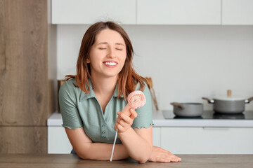 Young woman with small handheld electric fan in kitchen © Pixel-Shot