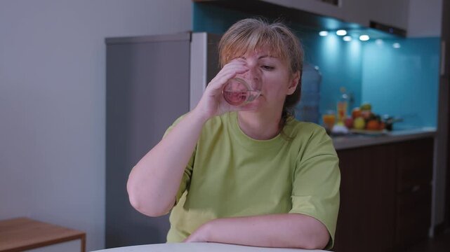 A woman drinks water from a glass cup, quenches her thirst