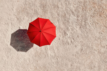 Top view of a single red umbrella on sandy beach creating strong contrast and shadow, representing summer, minimalism, heat, and solitude.