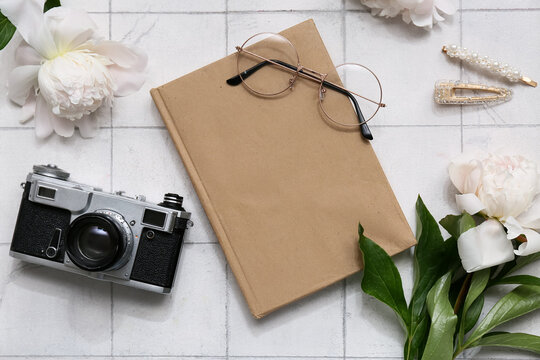 Composition with book, photo camera and peony flowers on white tile background