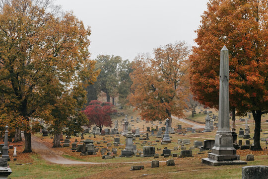 A cemetery surrounded by fall leaves and colorful trees in October.