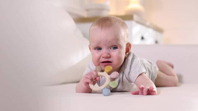 Cute little baby with teether on sofa at home