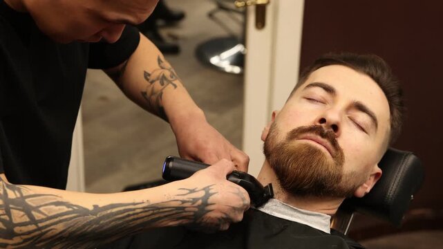 Stylist trimming man's beard with hair clipper in barbershop