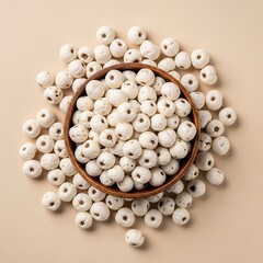 Puffed gorgon nuts with dark spots artistically scattered around a dark wood bowl on a tan surface.