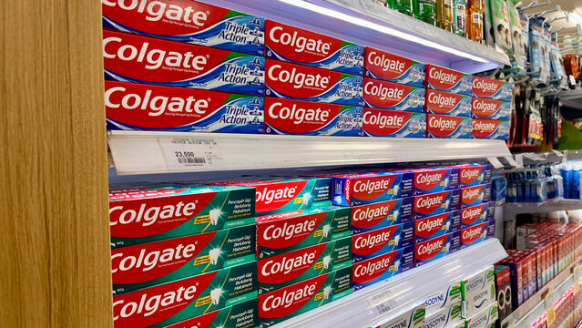 A supermarket shelf displays various Colgate toothpaste products in vibrant red and green packaging.