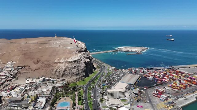 Aerial 4K view of Morro de Arica with Chilean flag waving, sunny day over the Pacific Ocean coast and historical landmark. Chile