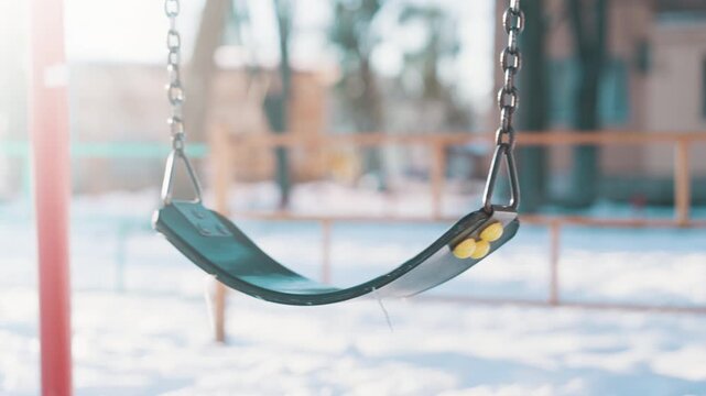 Empty Swing Swinging on Chain at Snowy Playground on Sunny Winter Day | Slow Motion Close-Up of Abandoned Kids Swing Seat Outdoors | Cold Season Childhood Scene