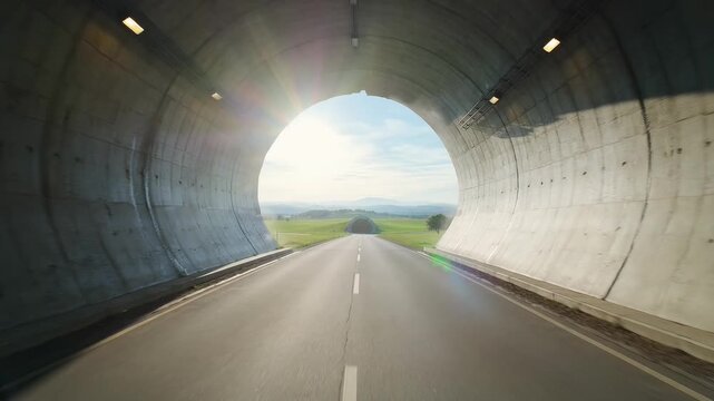 A car exits a tunnel onto a road with greenery and a bright sky ahead.