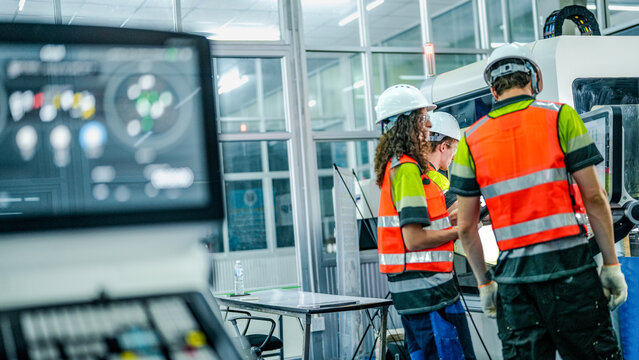 Three engineers program an industrial robot or 5-axis CNC machine using an AI interface. The team manufactures advanced microchips or high-tech components in a smart factory.