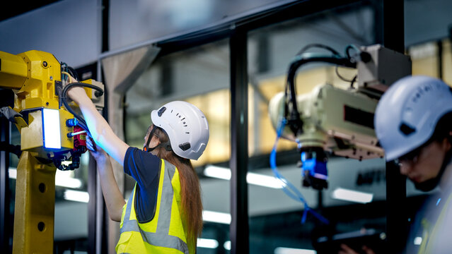 Two female robotics engineers in an R and D lab test an artificial intelligence cobot. They are inspecting the robotic system hardware, sensors, and programming.