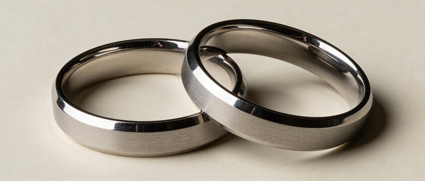 Close-up shot of two intertwined silver wedding bands with matte and polished finishes on a light background.