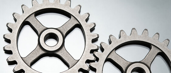 Close-up shot of two steel gears meshing together against light background, symbolizing mechanism and teamwork.