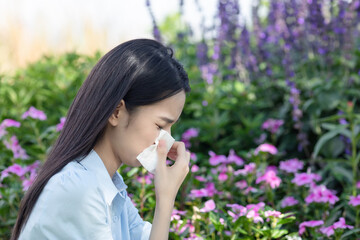 A young woman experiencing nasal allergies beside a flower bush