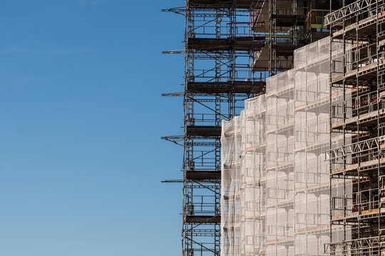 Urban architecture renovation with building facade wrapped in scaffolding and netting under clear sky showing construction structure and work progress