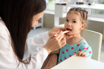Female pediatrician checking little girl's throat in clinic