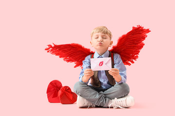 Naklejka premium Cute little happy boy in cupid wings with gift boxes and love letter blowing kiss on pink background. Valentine's Day celebration