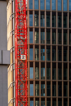 Urban construction industry scene with tall building facade and windows beside a red crane showing steel architecture and strong vertical design