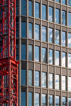 Modern urban architecture with glass office building facade and windows next to a red crane showing active construction and contemporary design