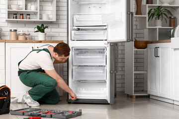 Male worker with tools repairing refrigerator in kitchen