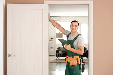 Male worker with electric drill repairing door at home