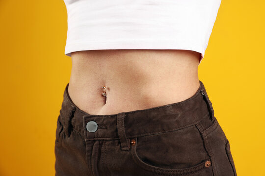 Woman with belly button piercing on yellow background, closeup
