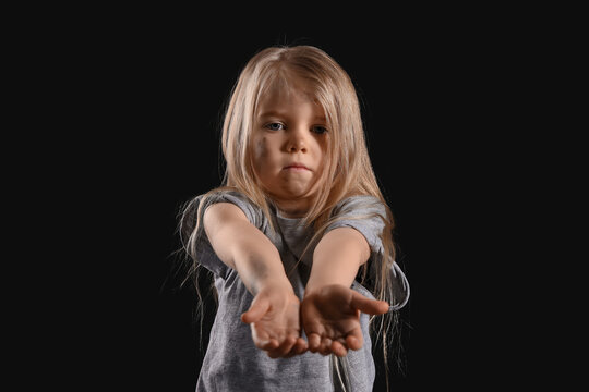 Homeless little girl begging for money on dark background