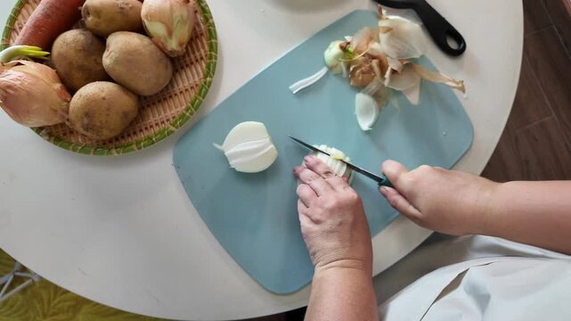 Close-up of female hands cutting onions with a sharp kitchen knife on a cutting board