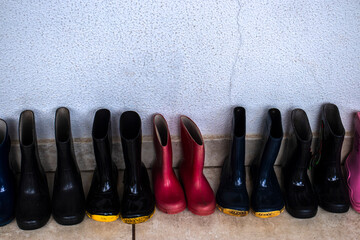 Row of small children's pink and black rubber rain boots lined up in a Brazilian preschool hallway. Organized waterproof footwear ready for kids' outdoor play on a rainy school day.