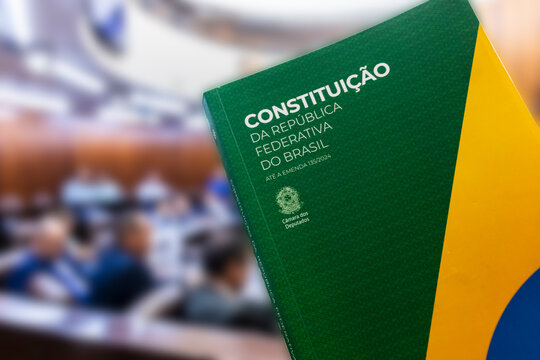 The Brazilian Federal Constitution, updated to amendment 135/2024, in focus. Municipal council plenary session is blurred in the background, symbolizing law and democracy in Brazil.