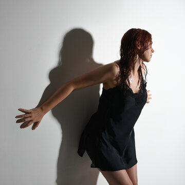 Close portrait of girl model, wet messy hair wearing simple black silk robe gown, standing pose leaning against a wall with strained emotive pose. Isolated figure with shadows on studio background.