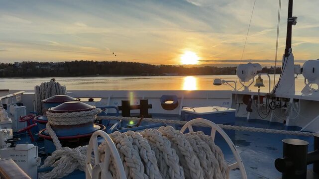 Bright sun setting over the water with golden reflections on the deck and railing of a moving ship or boat.