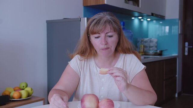 Woman eats a peeled red apple, sits at a table
