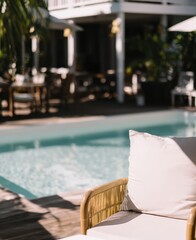Obraz premium Modern wicker lounge chair by a crystal clear resort pool. Sunny tropical hotel patio, summer vacation tourism, and high-end hospitality relaxation concept.