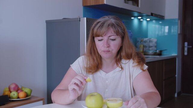 Woman eats a green apple in the background of a kitchen, close-up