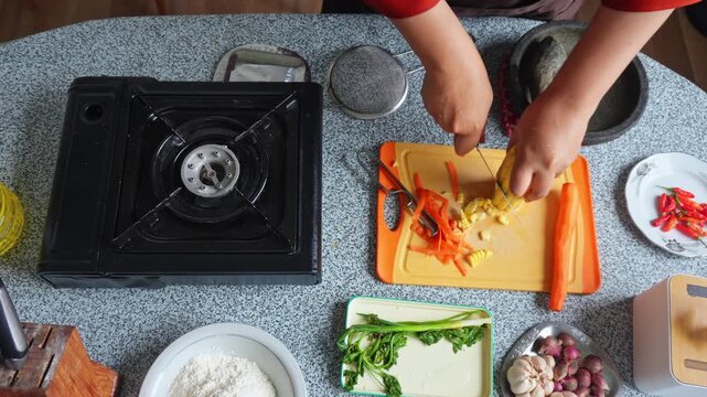 Top-down view of person slicing fresh corn kernels off cob on cutting board for Indonesian corn fritters (Bakwan Jagung)