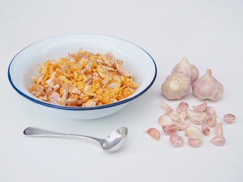 Golden fried garlic is in a bowl placed on a white surface.