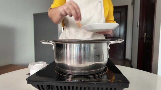 In the kitchen, a woman's hands dip a chicken fillet into a pot of boiling water.