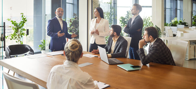 Business leader speaking on office meeting in front of diverse team of corporate employees. Idea and task presentation from senior boss at briefing, people listen important speech together