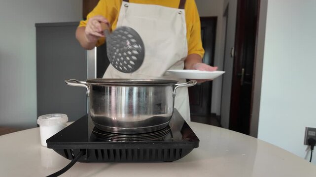 Boiling meat broth in a saucepan on an induction hob . A woman removes foam from the surface