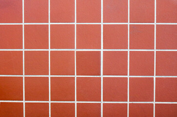 Fototapeta premium A neat arrangement of square terracotta tiles. The warm, reddish-brown clay features a fine, sandy texture and a matte finish.
